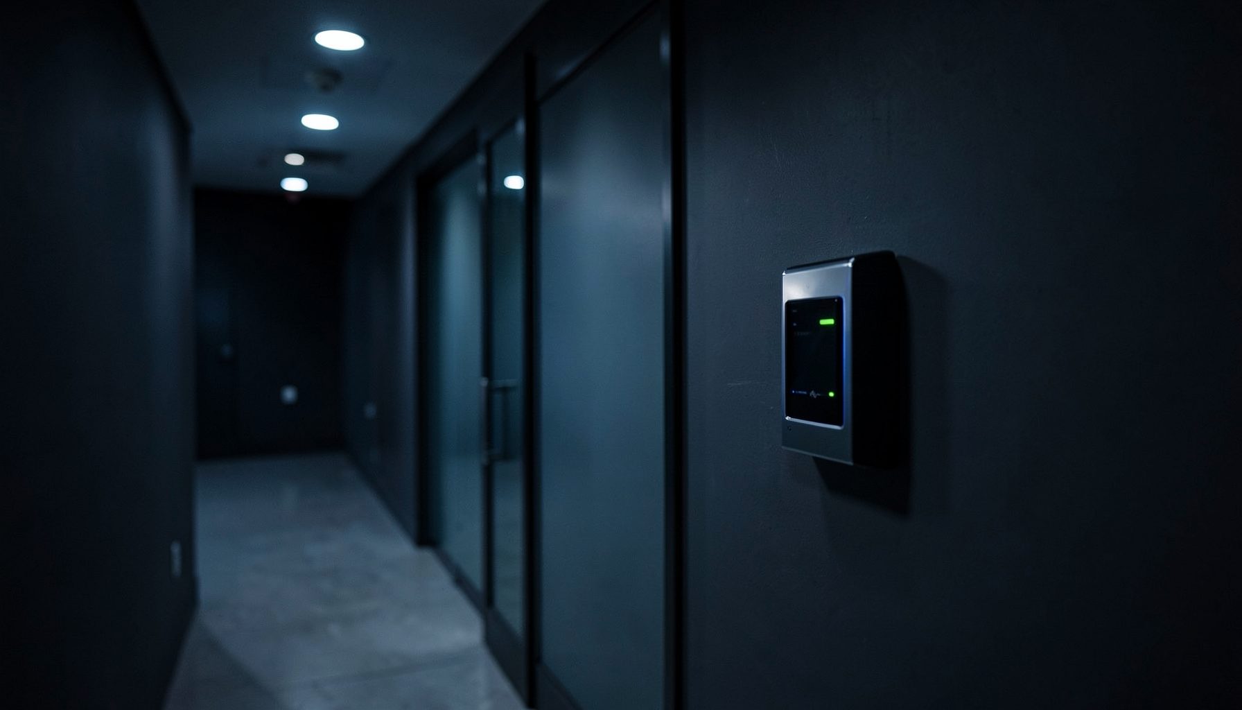 Darkened corridor with a sleek card reader mounted on the wall beside a glass door, cool blue-gray tones and soft overhead lighting